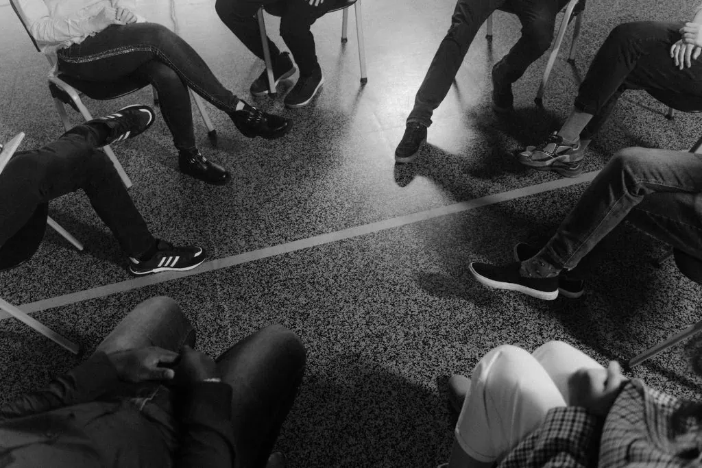 Black and white photo of people sitting in a circle during a group therapy or support session.