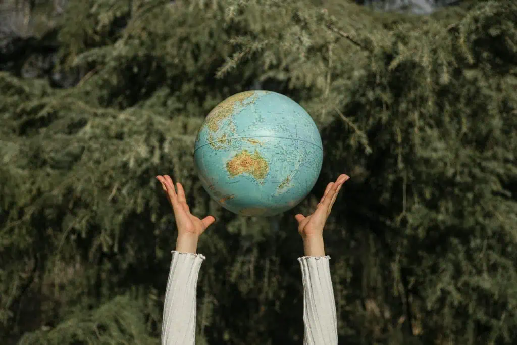 Person holding up a globe with both hands against a backdrop of green trees, symbolizing global connection, responsibility, and unity with nature.
