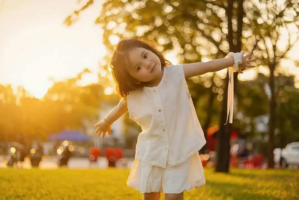 Young girl in white dress playing outdoors at sunset, representing the joy and energy that can sometimes be mistaken for ADHD symptoms in children.