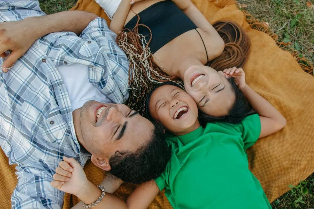 Joyful family lying on a picnic blanket outdoors, laughing and enjoying quality time together on a sunny day.