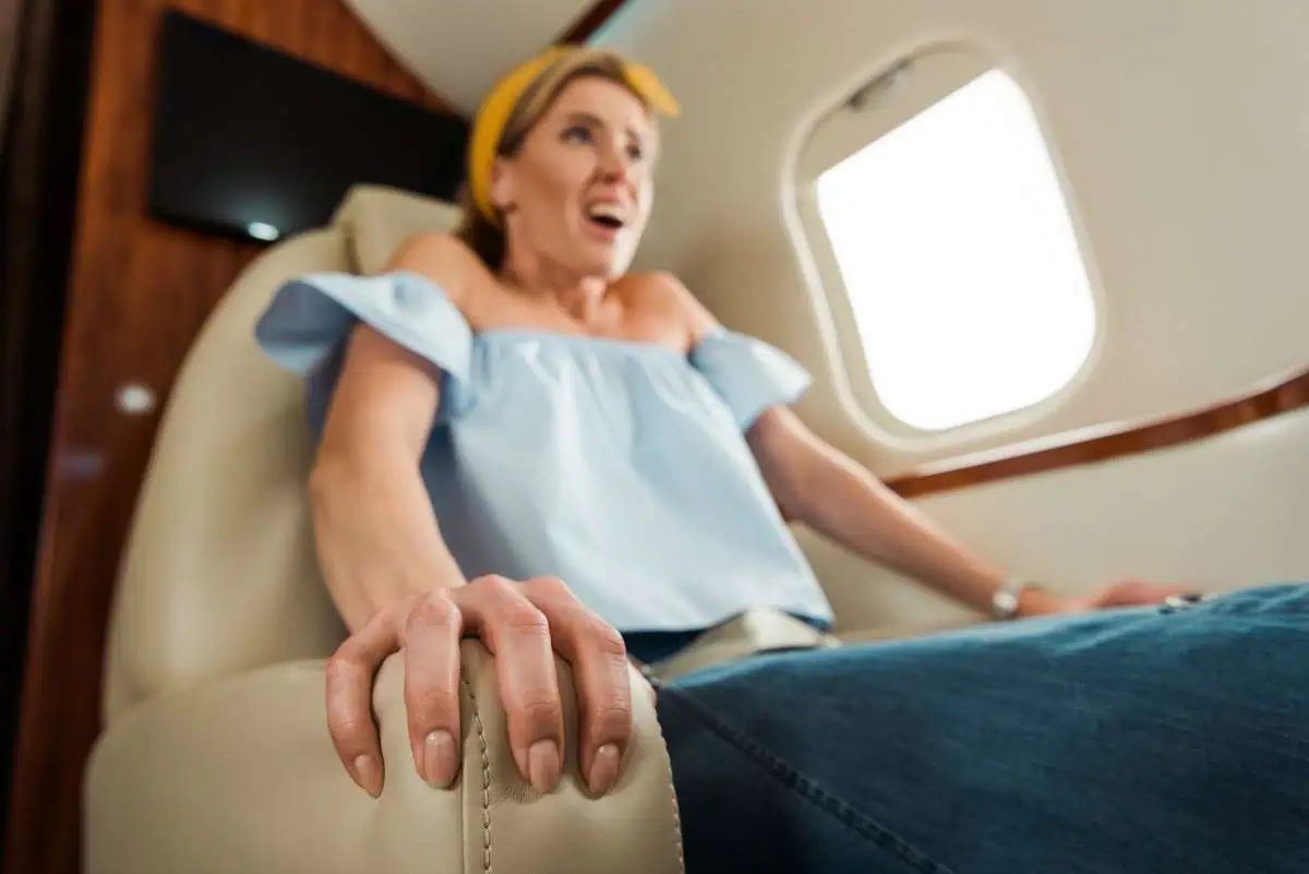 Nervous woman gripping airplane seat armrest during flight, showing signs of fear of flying