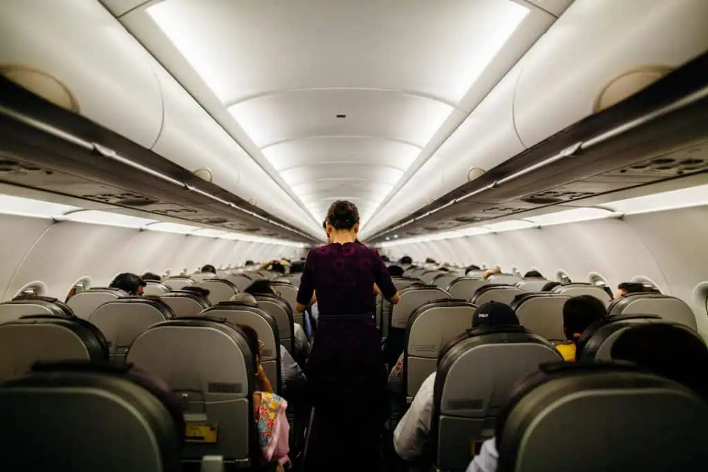 Flight attendant walking down the aisle of a full airplane cabin during flight