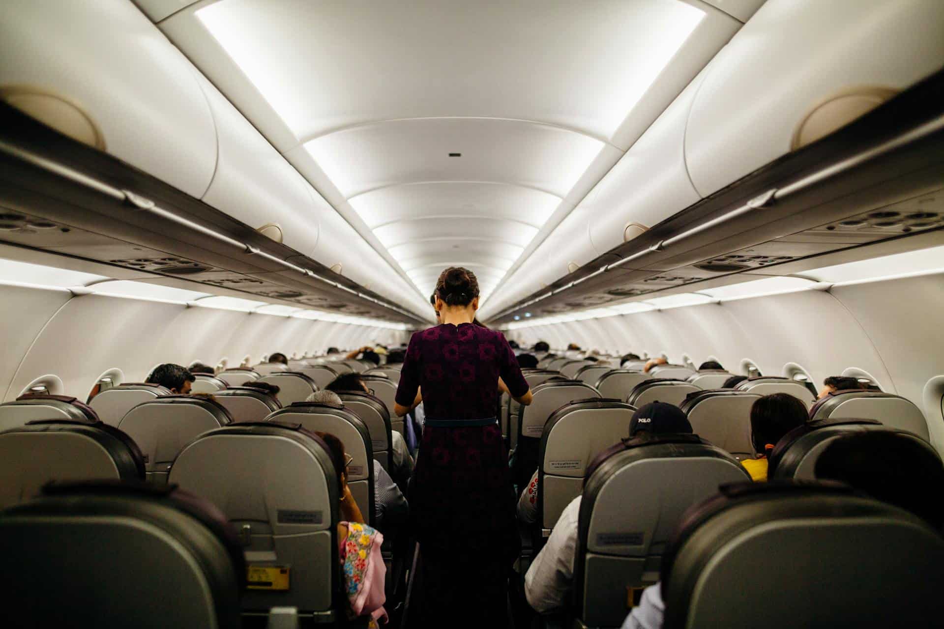 Flight attendant walking down the aisle of a full airplane cabin during flight