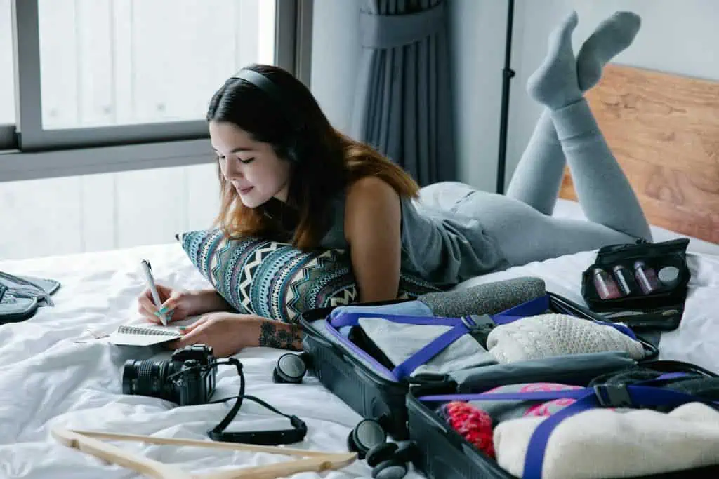 Woman journaling on bed with suitcase open, using mindfulness techniques to reduce pre-flight anxiety