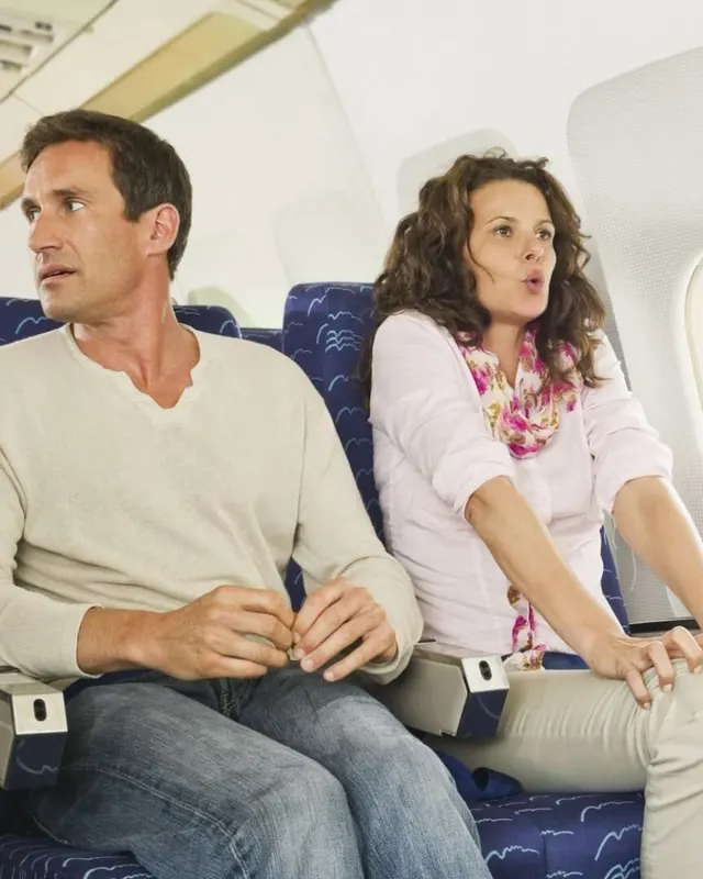 A man and a woman in aeroplane seats looking tense and alert