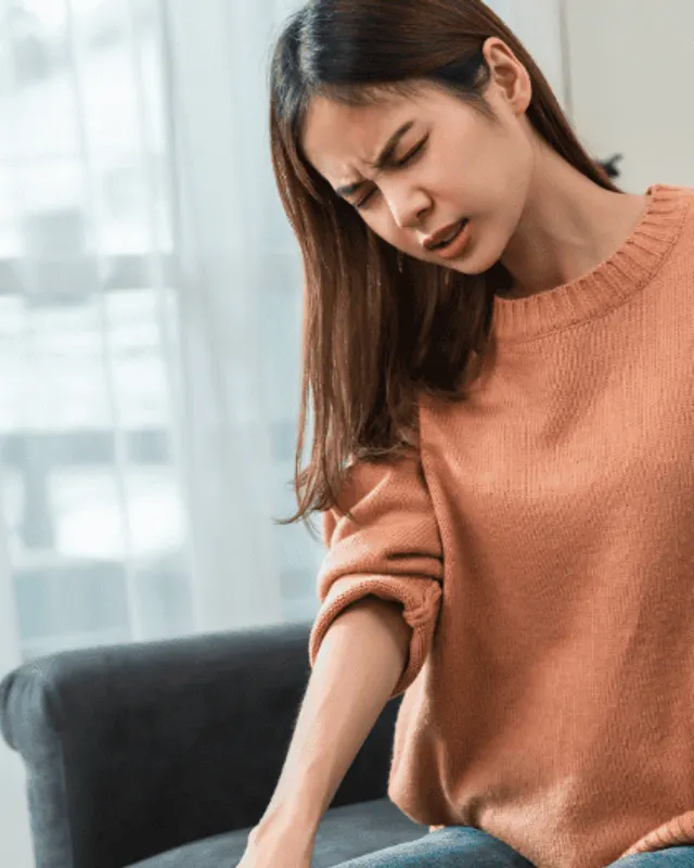 Woman sitting on a sofa pressing a hand to her lower back with a pained expression