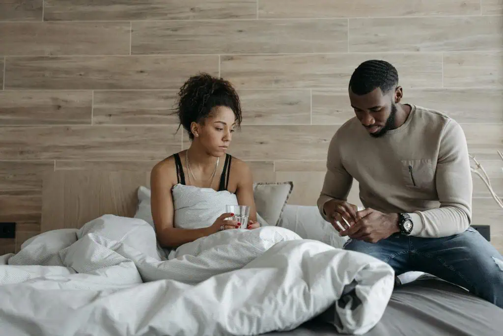 Man helping a woman in bed who appears unwell, offering support possibly for a morning headache