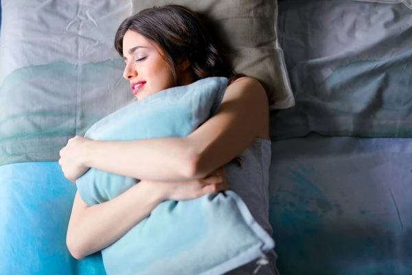 sleep hygiene_Hypnotherapy for Better Sleep: A woman peacefully sleeping while hugging a pillow in a cozy bedroom.