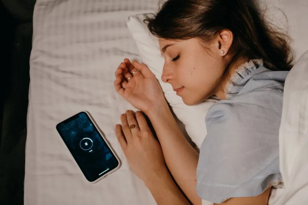 Hypnotherapy for sleep: A woman peacefully sleeping on a bed while listening to a guided hypnosis session on her smartphone.