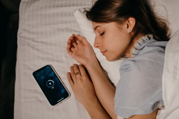Strategic Hypnotherapy: How to Achieve Restorative Sleep Naturally Hypnotherapy for sleep: A woman peacefully sleeping on a bed while listening to a guided hypnosis session on her smartphone.