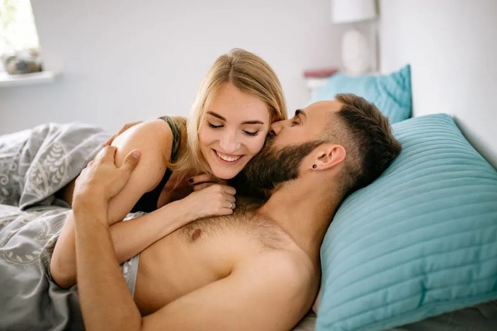 A happy couple in bed, smiling and embracing intimately while enjoying a loving moment together.
