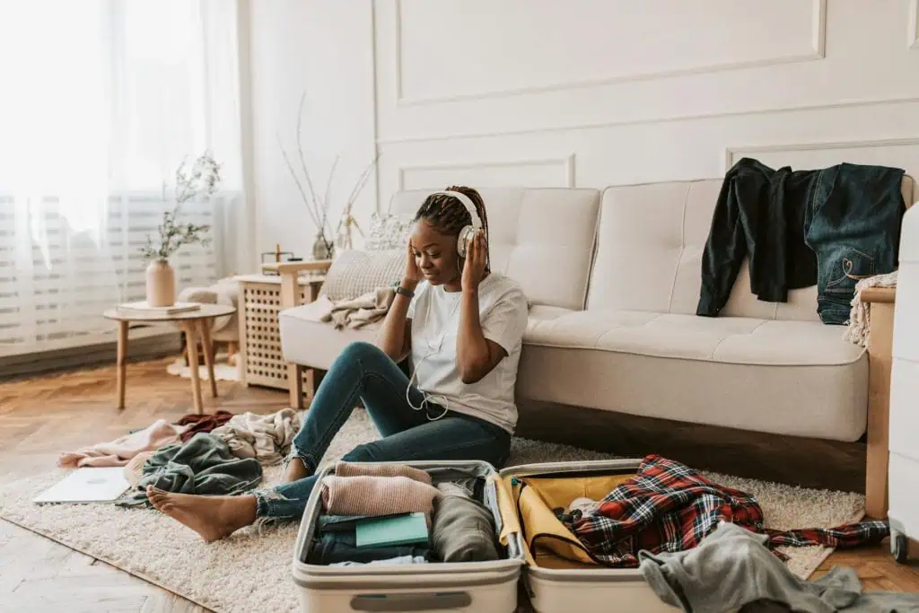 Young woman listening to music while packing her suitcase, practicing relaxation before a flight