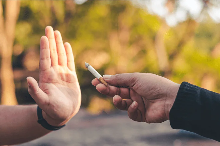 A person rejecting a cigarette offer with a raised hand gesture.