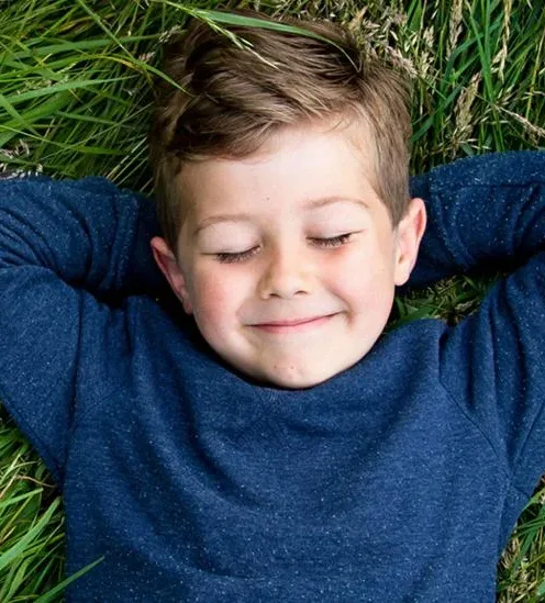 Boy lying in long grass with his hands behind his head, eyes closed and smiling