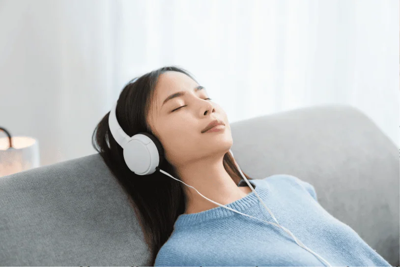 Bearded man lying on the floor with eyes closed, wearing headphones and holding a smartphone, appearing relaxed and peaceful.