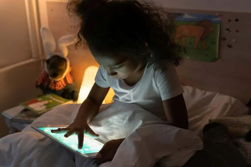 Young child using a tablet in bed at night, highlighting the effects of screens and ADHD on sleep and focus.