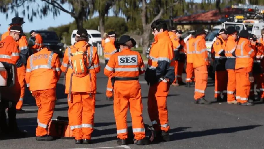 Group of emergency response personnel wearing bright orange uniforms labeled "SES" standing together in a street setting.