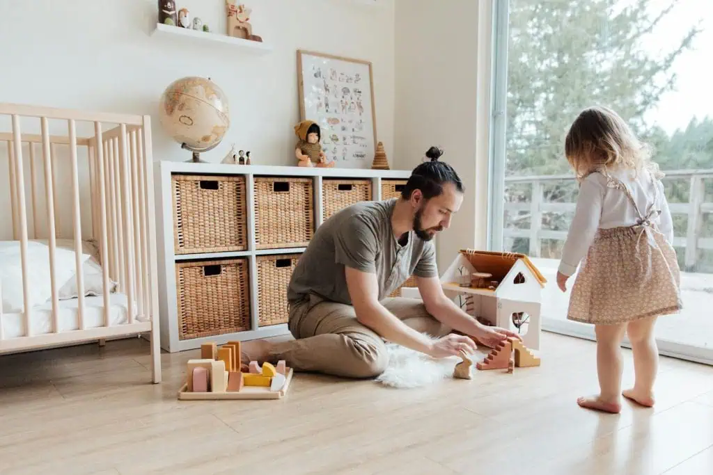 A father sitting on the floor playing with his young daughter in a bright, organized room, symbolizing hands-on solo parenting after separation.