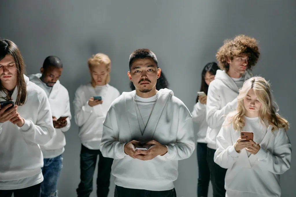 Group of young adults wearing white hoodies, standing together while focused on their smartphones, symbolizing smartphone addiction.