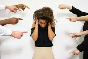 A distressed woman covering her ears while multiple hands point at her, symbolizing social anxiety and fear of judgment.