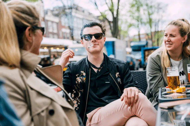 A group of friends socializing outdoors, with one person smoking a cigarette.