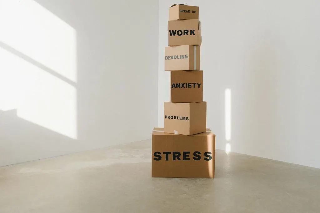 Stack of cardboard boxes labeled with stress-related words like anxiety, work, and problems, symbolizing emotional overload
