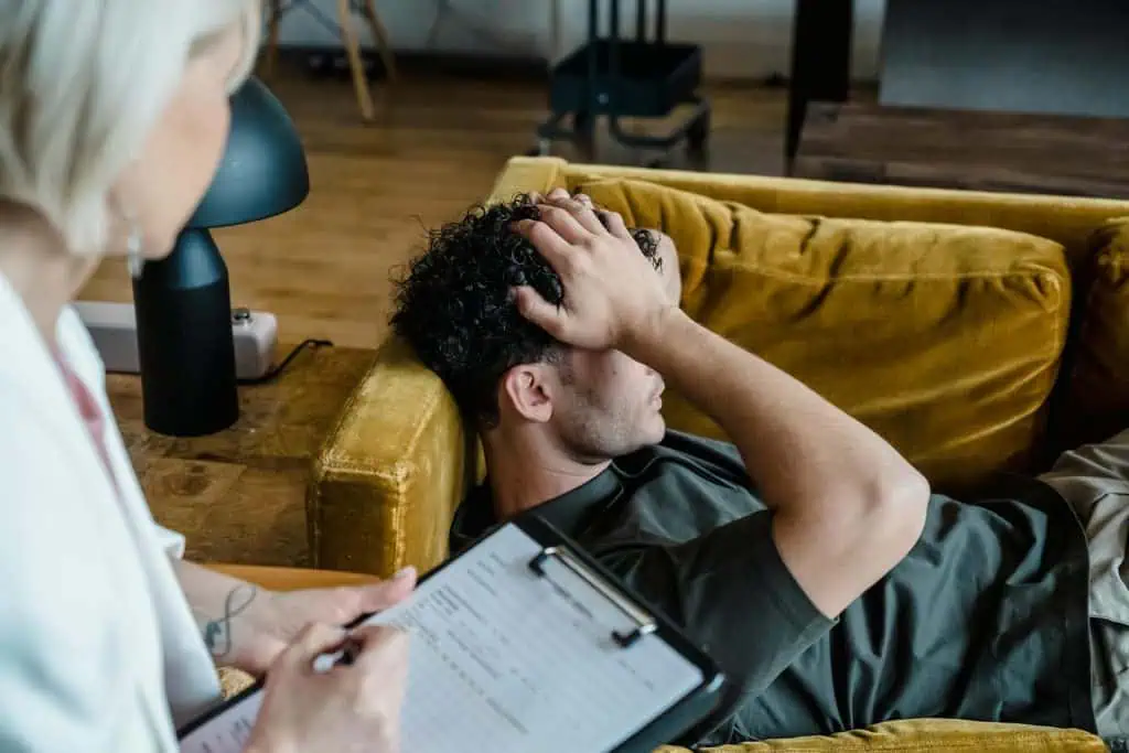 A man lying on a sofa with a distressed expression during a therapy session, symbolizing emotional support through hypnotherapy.
