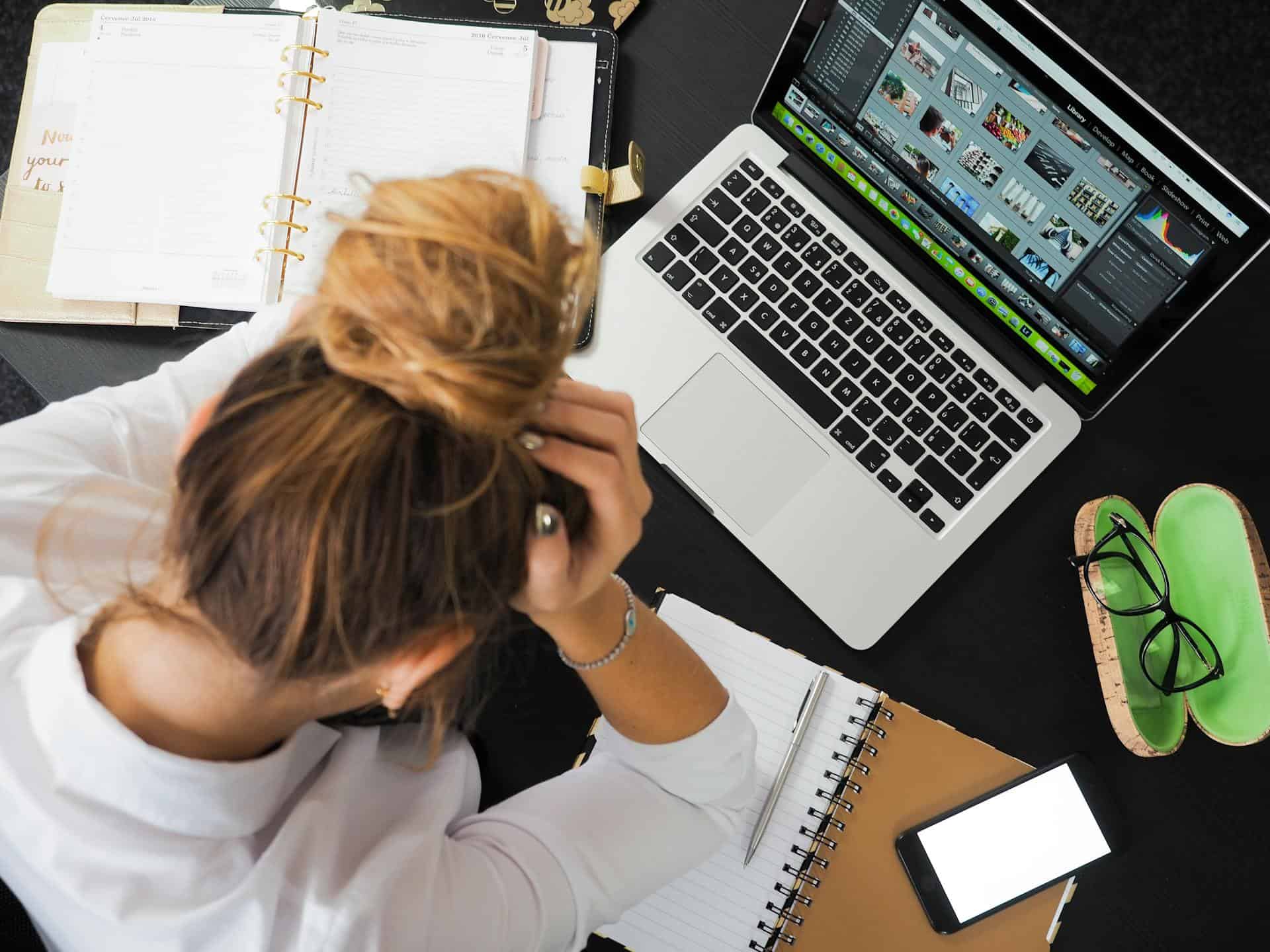 Woman at a desk with a planner and laptop, head in her hands
