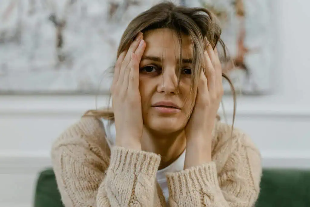 Young woman with a tired expression holding her head in her hands, showing signs of stress, fatigue, or emotional overwhelm.