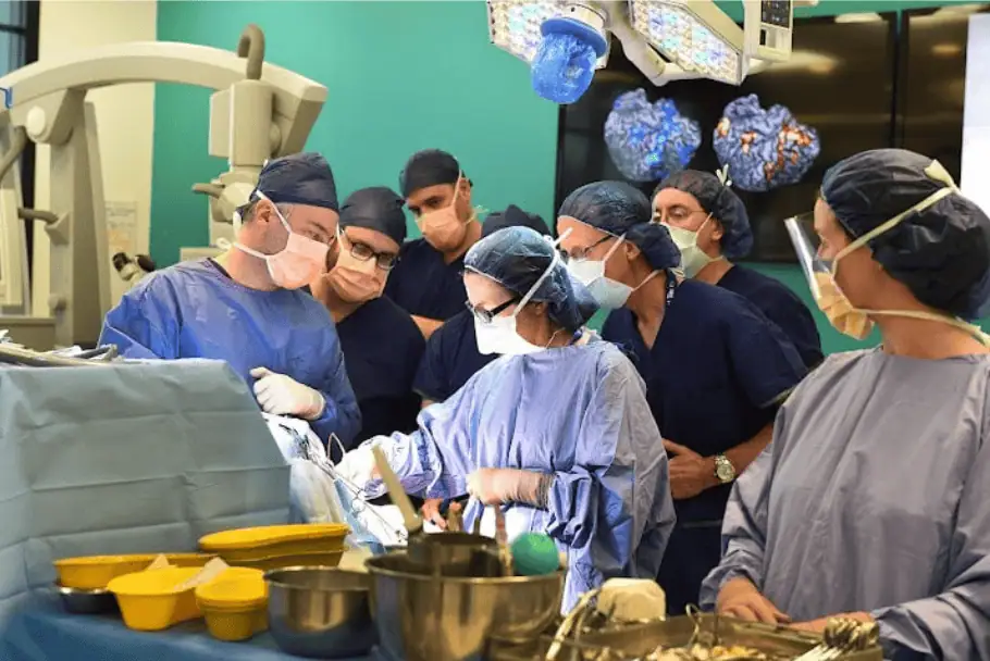 A team of surgeons and medical professionals in an operating room performing surgery under bright lights.