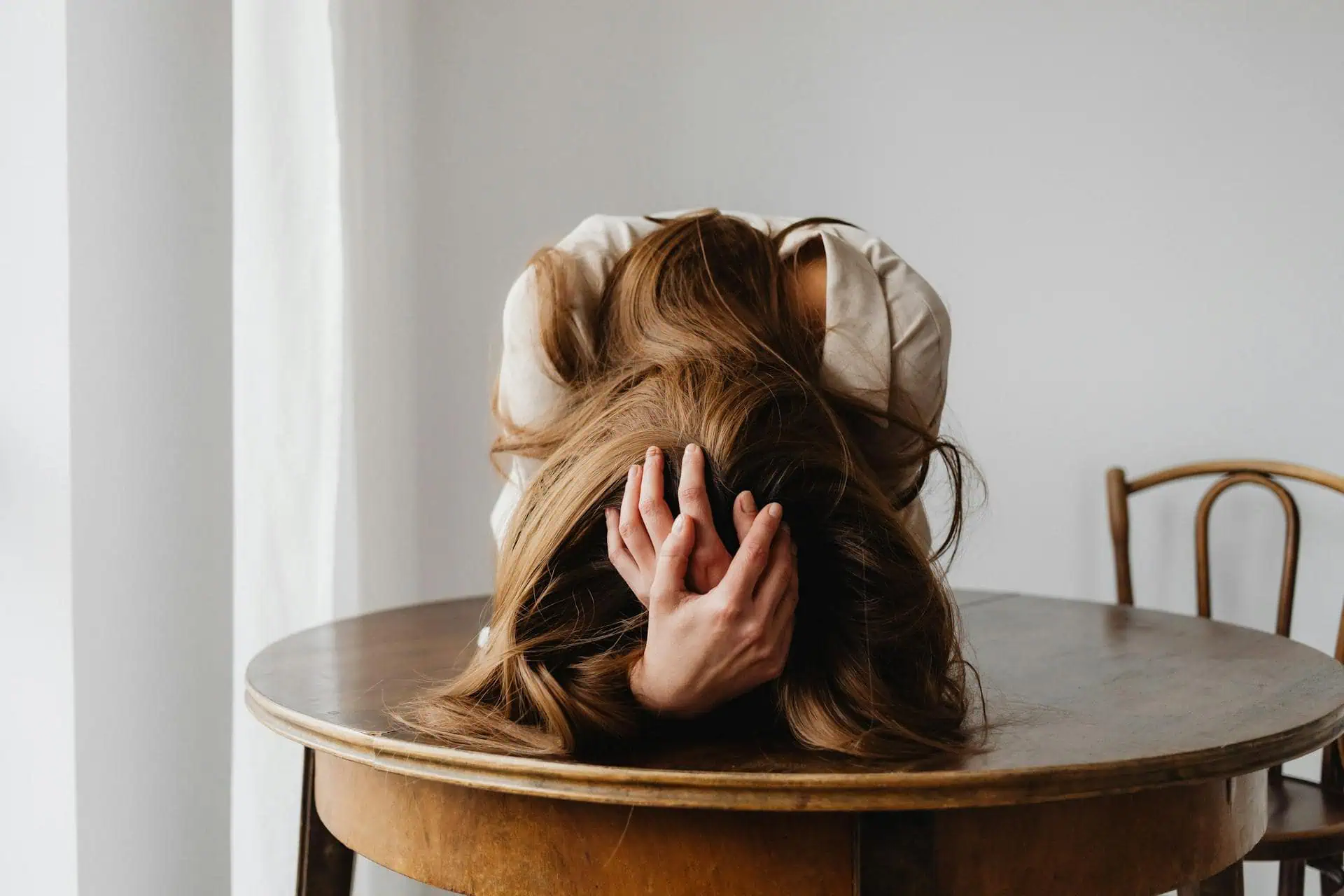 Teen girl with her head down on a table, holding her hair in distress, expressing signs of emotional overwhelm and stress.