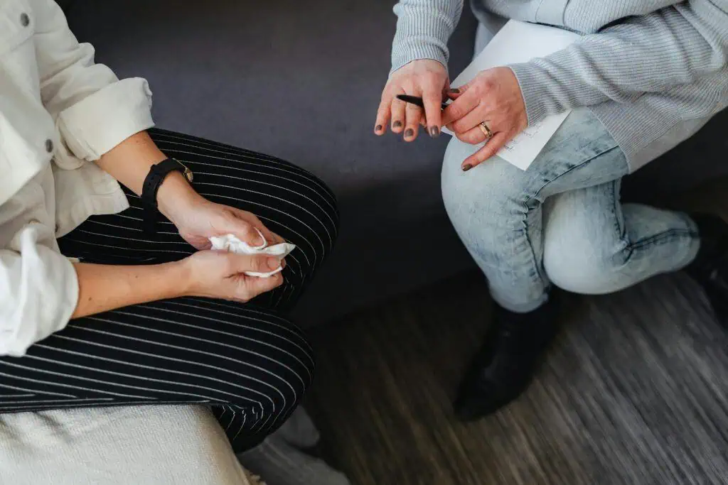 A close-up of two people during a therapy session, one person holding a tissue and the other holding a pen and paper, capturing a moment of emotional support.