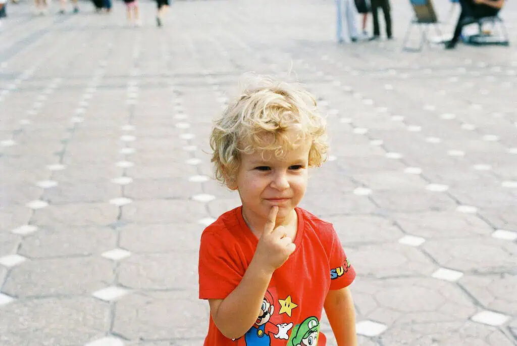 Blonde-haired young boy in a red shirt standing outdoors, symbolizing curiosity and the need to understand ADHD symptoms in children.