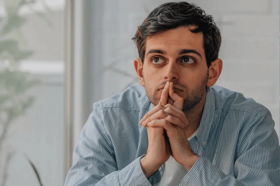 Thoughtful man staring upward with hands together, appearing deep in contemplation or worry.