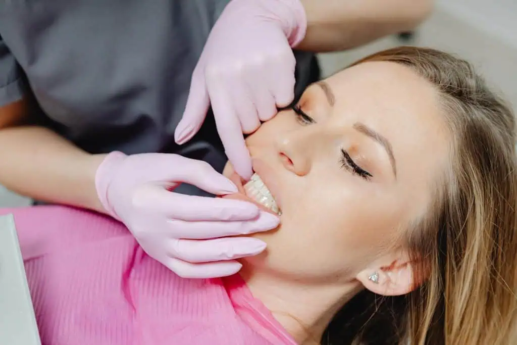 A woman receiving a dental examination with pink-gloved hands checking her jaw and bite alignment, commonly part of TMJ disorder evaluation.