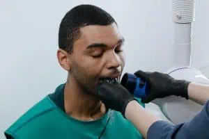 A patient undergoing a dental X-ray examination to diagnose TMJ disorder, assisted by a professional wearing black gloves.