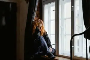 A woman sitting by the window appearing emotionally distressed, possibly experiencing TMJ disorder in women.