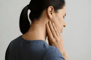 Woman touching her jaw and neck, illustrating discomfort caused by TMJ and poor posture