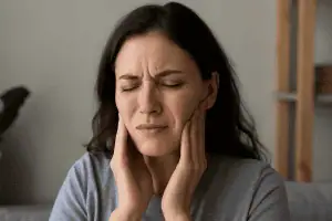 A young woman pressing her hands against her jaw with a pained expression, showing signs of TMJ or bruxism-related jaw pain.