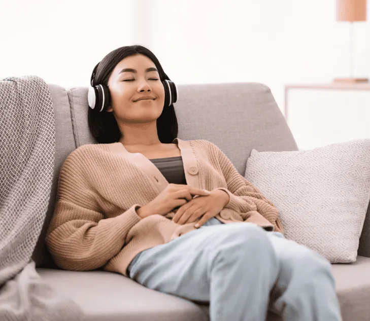 A young woman wearing headphones, relaxing on a cozy sofa with a peaceful smile, enjoying music or a guided meditation.