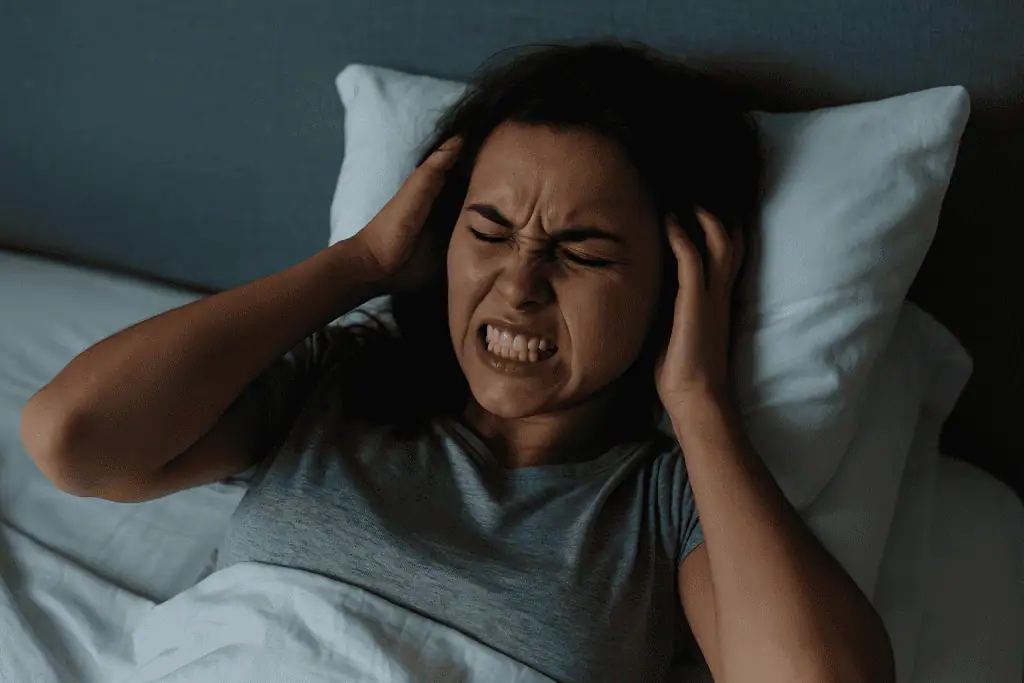 Woman lying in bed with eyes shut and teeth clenched, showing visible signs of stress and nighttime teeth grinding (bruxism).
