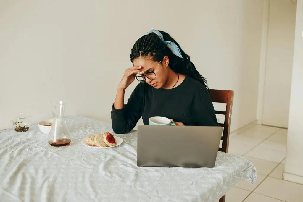 Woman holding her head while working on a laptop, possibly experiencing a morning headache from sleep bruxism or poor sleep.